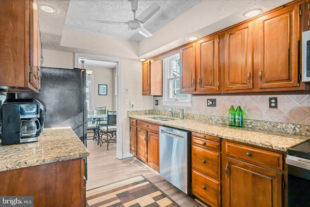 kitchen featuring light wood-type flooring, light stone counters, appliances with stainless steel finishes, and a textured ceiling