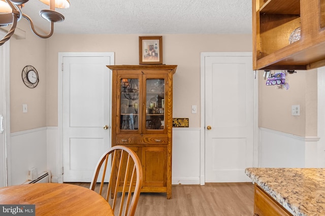 dining room featuring a baseboard heating unit, light hardwood / wood-style floors, and a textured ceiling