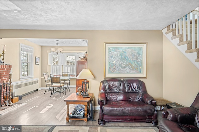 living room with a textured ceiling, radiator, a notable chandelier, a brick fireplace, and light hardwood / wood-style flooring