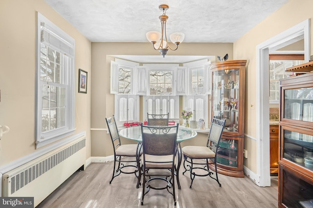 dining room featuring a chandelier, light wood-type flooring, radiator heating unit, and a textured ceiling