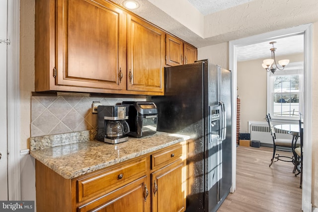 kitchen featuring light stone countertops, radiator heating unit, an inviting chandelier, decorative backsplash, and light wood-type flooring