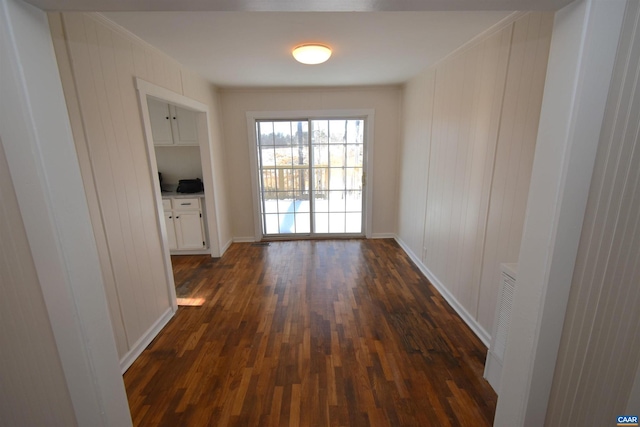 hall with ornamental molding, wooden walls, and dark wood-type flooring