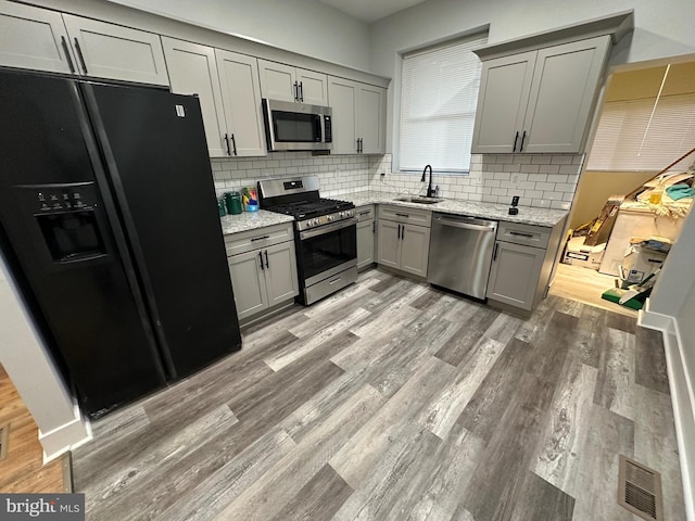 kitchen featuring light stone countertops, backsplash, gray cabinetry, and stainless steel appliances