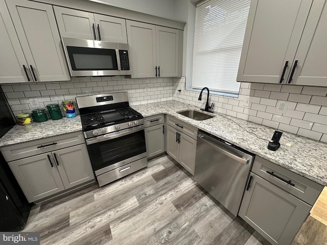 kitchen with light hardwood / wood-style flooring, appliances with stainless steel finishes, sink, gray cabinets, and decorative backsplash