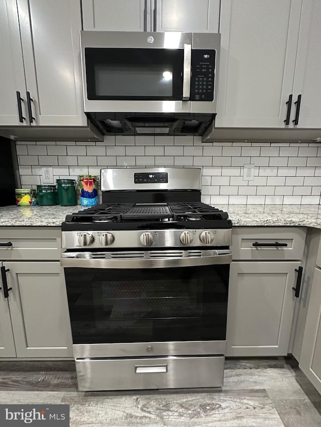 kitchen featuring light stone countertops, appliances with stainless steel finishes, light wood-type flooring, and tasteful backsplash