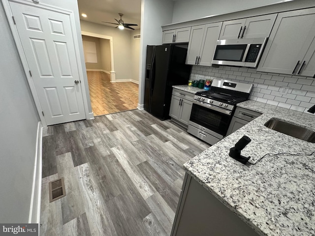 kitchen with light stone countertops, appliances with stainless steel finishes, tasteful backsplash, sink, and light wood-type flooring