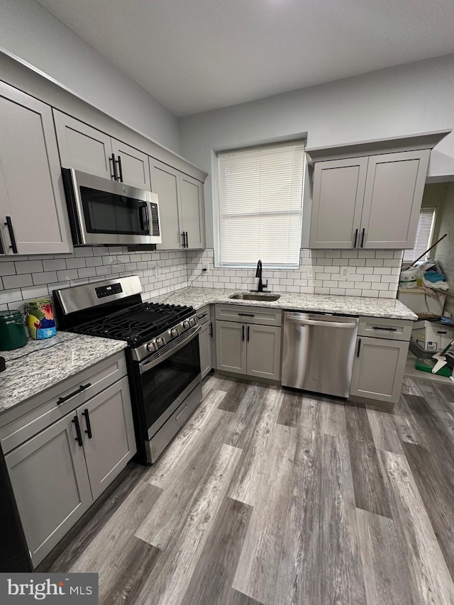 kitchen with sink, light stone counters, gray cabinetry, and appliances with stainless steel finishes