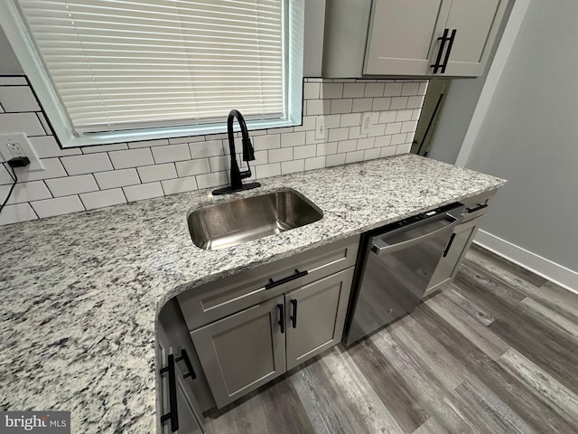 kitchen with stainless steel dishwasher, dark hardwood / wood-style flooring, sink, light stone counters, and decorative backsplash