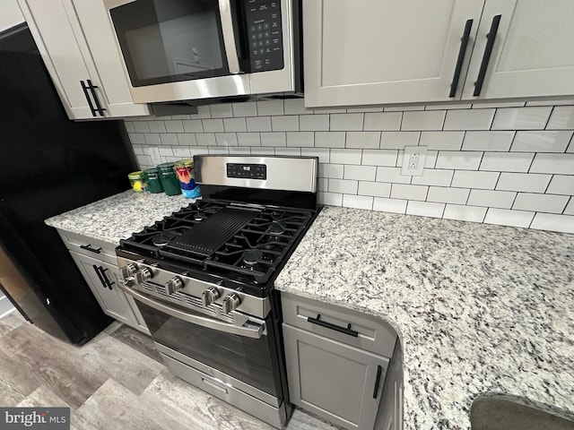 kitchen featuring light stone countertops, decorative backsplash, light hardwood / wood-style flooring, stainless steel appliances, and gray cabinets