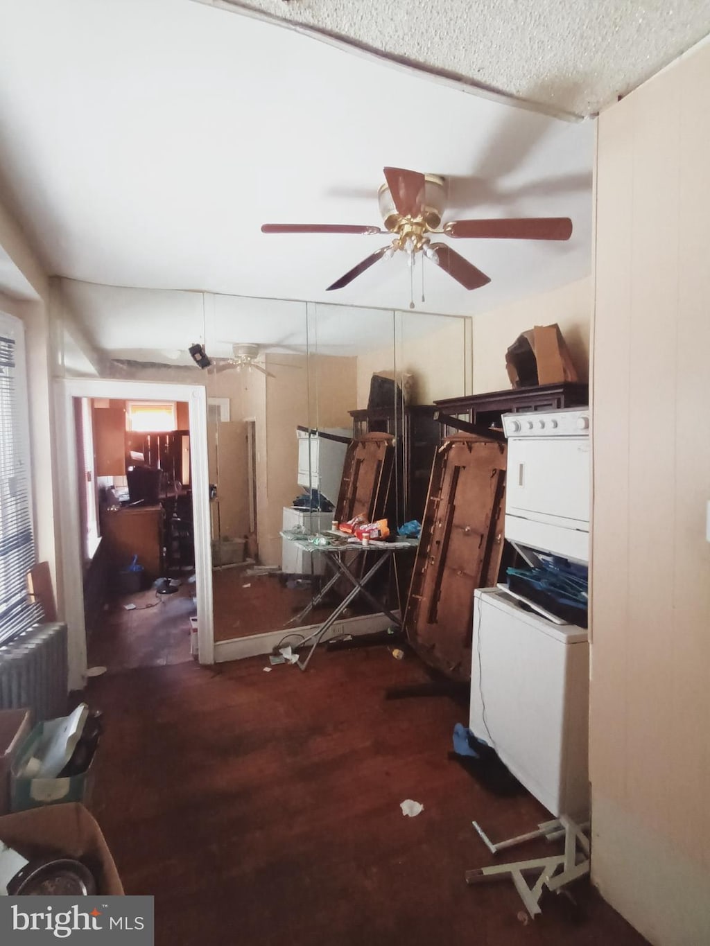 miscellaneous room with ceiling fan, dark wood-type flooring, radiator, and stacked washer / drying machine