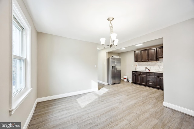 kitchen with dark brown cabinetry, stainless steel refrigerator with ice dispenser, decorative backsplash, hanging light fixtures, and light hardwood / wood-style flooring