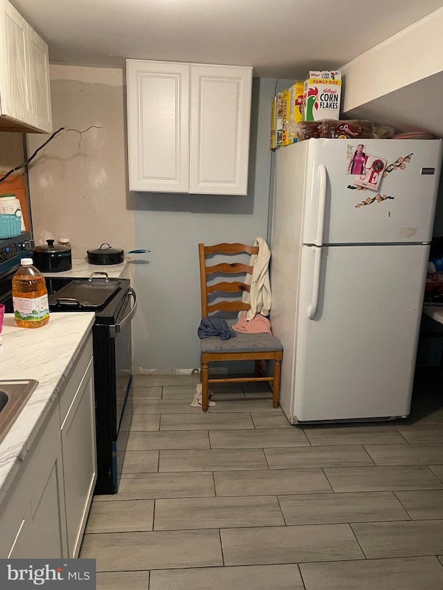 kitchen with white refrigerator, white cabinets, and black range with electric cooktop