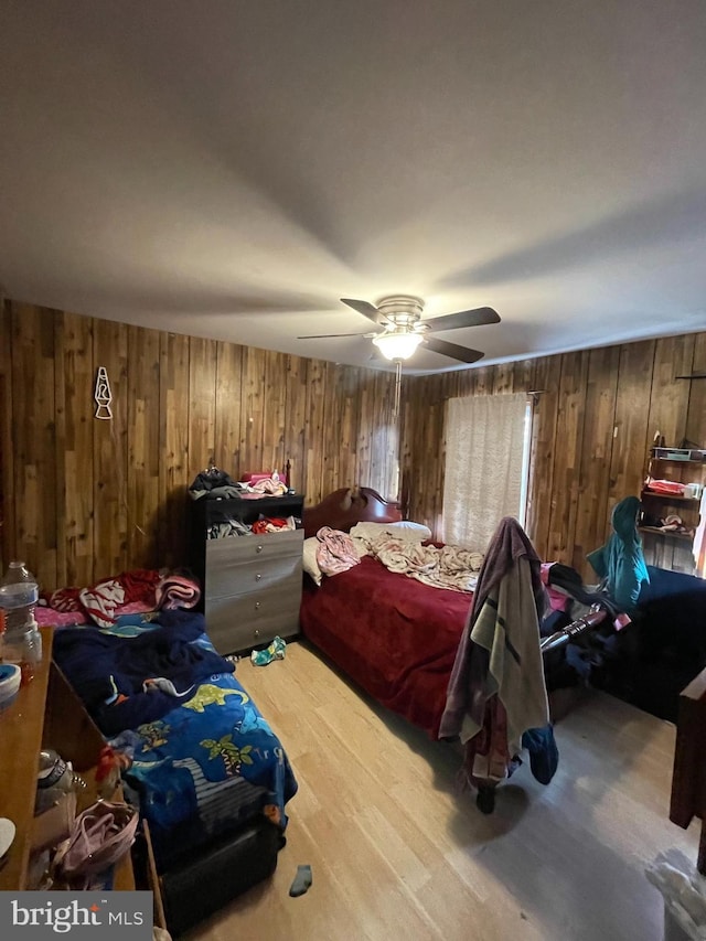 bedroom with ceiling fan, wood walls, and hardwood / wood-style floors