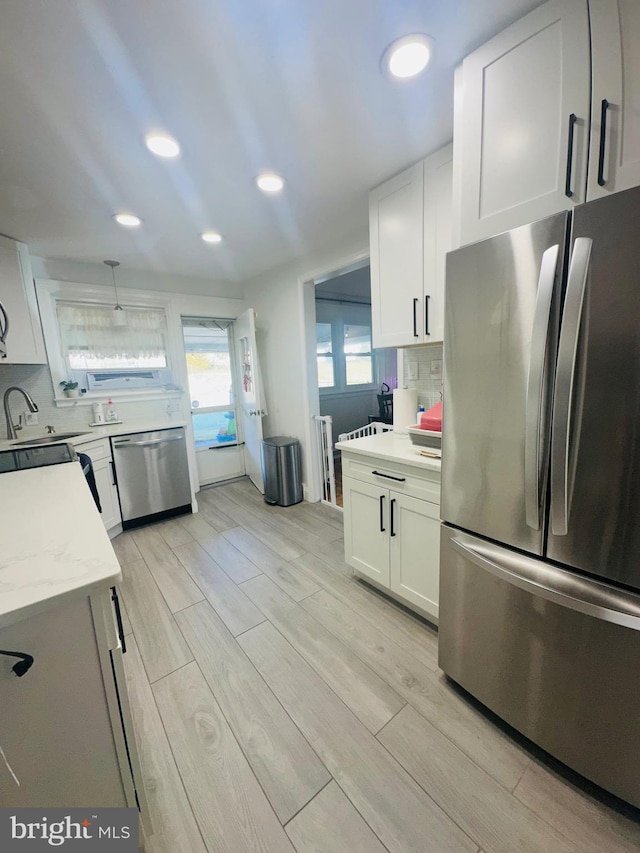 kitchen with tasteful backsplash, white cabinetry, sink, decorative light fixtures, and stainless steel appliances