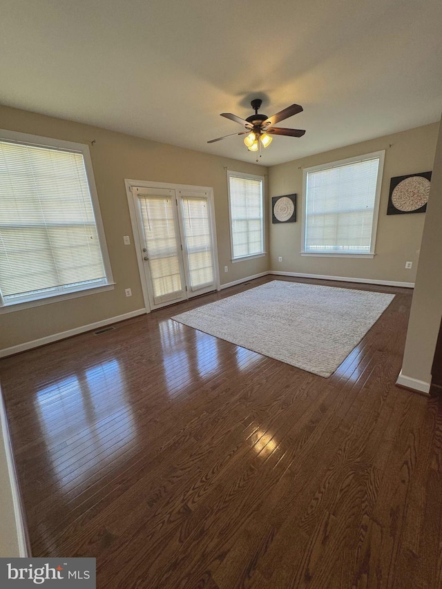 unfurnished living room featuring ceiling fan, baseboards, and dark wood-style flooring