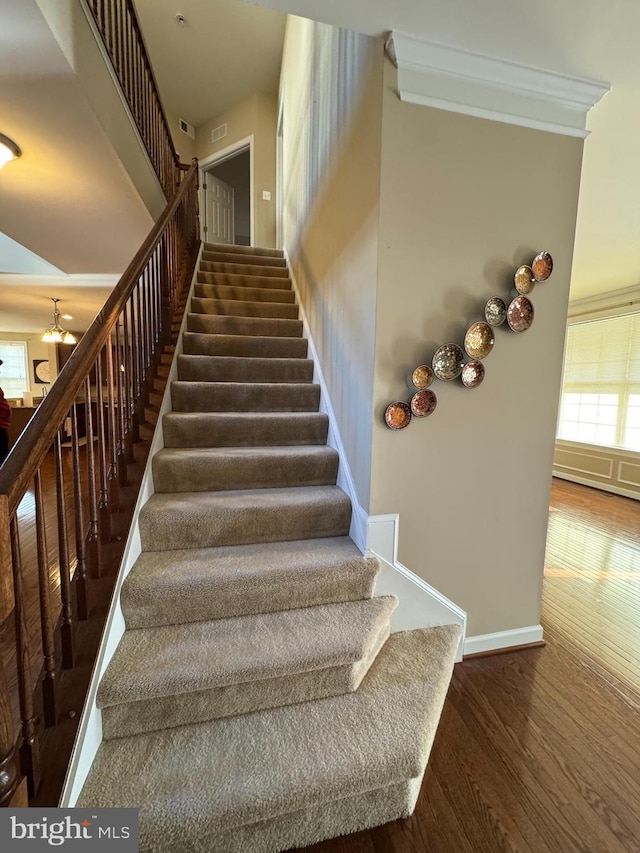 staircase with plenty of natural light, wood finished floors, baseboards, and ornamental molding