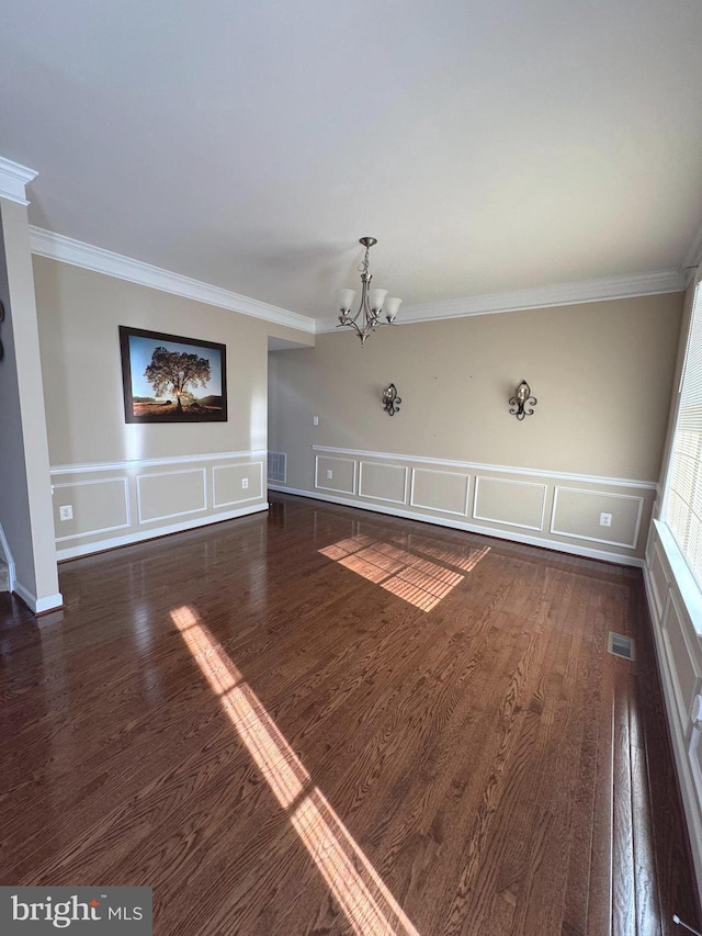 unfurnished living room with wood finished floors, visible vents, an inviting chandelier, crown molding, and a decorative wall