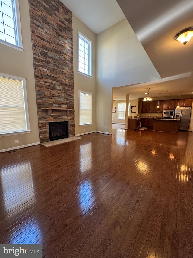 unfurnished living room featuring a fireplace, dark wood-style flooring, a towering ceiling, and baseboards