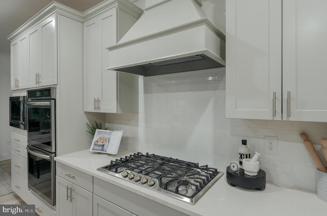 kitchen with premium range hood, white cabinetry, appliances with stainless steel finishes, and decorative backsplash