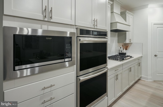 kitchen featuring appliances with stainless steel finishes, white cabinets, backsplash, custom range hood, and light wood-type flooring