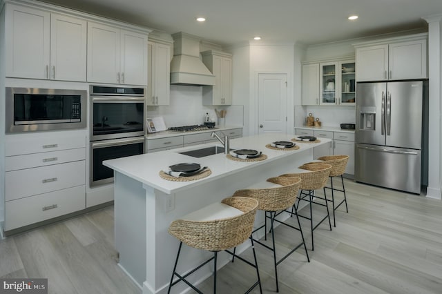 kitchen featuring appliances with stainless steel finishes, custom range hood, a kitchen island with sink, and a kitchen bar