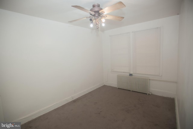 spare room with dark colored carpet, radiator, and ceiling fan