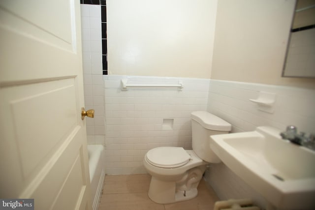 bathroom featuring a tub to relax in, toilet, sink, and tile walls