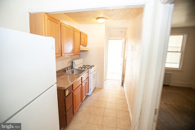 kitchen featuring sink, white appliances, radiator heating unit, light stone countertops, and light tile patterned flooring