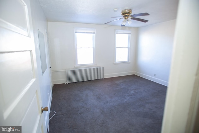 empty room with dark colored carpet, radiator, and ceiling fan