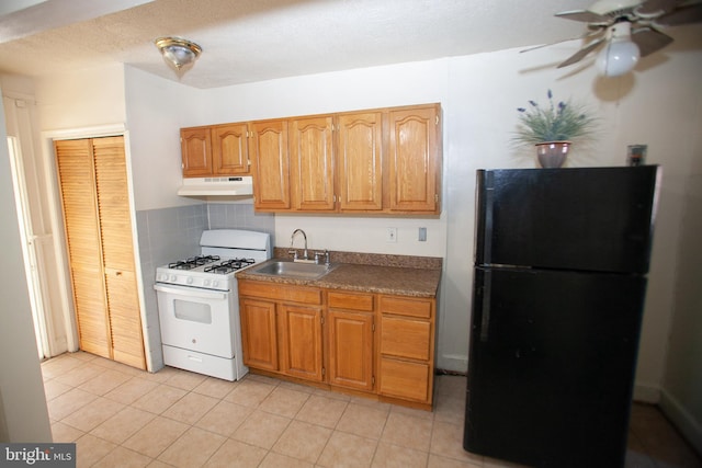 kitchen featuring sink, light tile patterned floors, gas range gas stove, black refrigerator, and backsplash