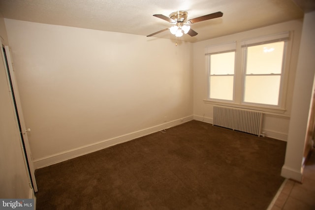 empty room featuring dark colored carpet, radiator heating unit, and ceiling fan