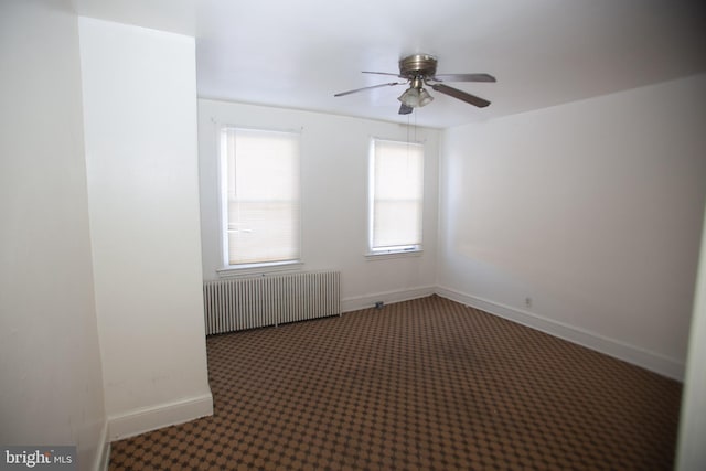 empty room featuring ceiling fan, radiator heating unit, and dark carpet