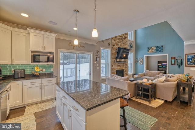 kitchen with a kitchen breakfast bar, stainless steel microwave, white cabinets, dark hardwood / wood-style flooring, and dark stone counters