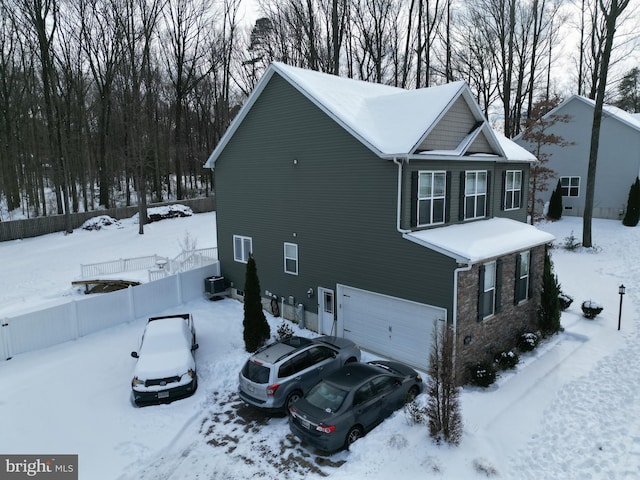 snow covered property with cooling unit and a garage