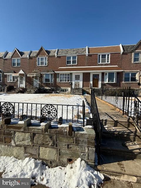 snow covered back of property with brick siding, fence, and a residential view