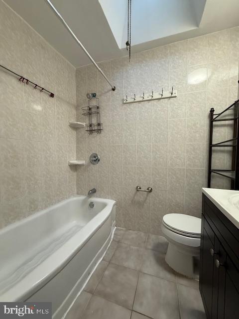 full bathroom with toilet, tile walls, tile patterned flooring, vanity, and tiled shower / bath