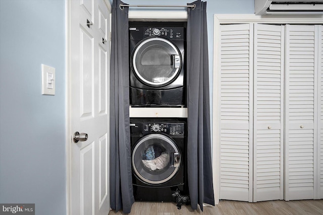 laundry room featuring stacked washing maching and dryer, an AC wall unit, and light hardwood / wood-style flooring