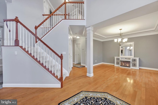 foyer with crown molding, hardwood / wood-style floors, a chandelier, and ornate columns