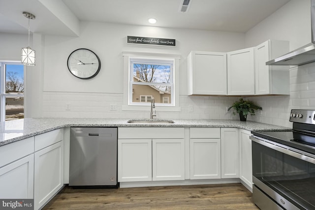 kitchen with light stone countertops, white cabinetry, stainless steel appliances, and wall chimney exhaust hood