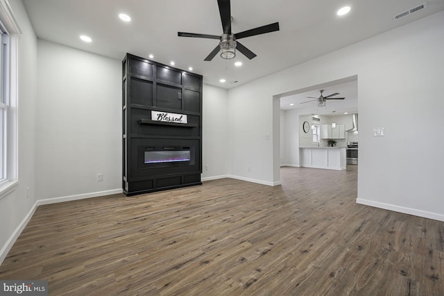 unfurnished living room featuring ceiling fan, dark wood-type flooring, and a large fireplace