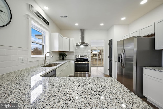 kitchen with light stone countertops, appliances with stainless steel finishes, white cabinets, wall chimney range hood, and sink