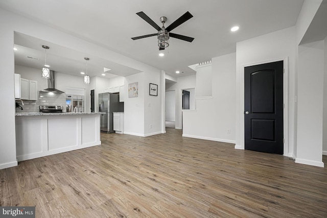 kitchen featuring white cabinetry, decorative backsplash, kitchen peninsula, stainless steel appliances, and wall chimney exhaust hood