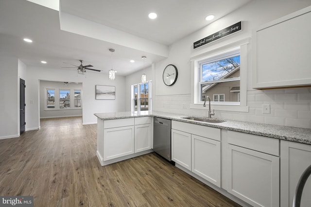 kitchen with light stone countertops, white cabinetry, sink, kitchen peninsula, and stainless steel dishwasher