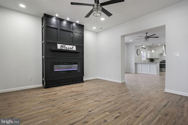 unfurnished living room featuring ceiling fan, a fireplace, and wood-type flooring