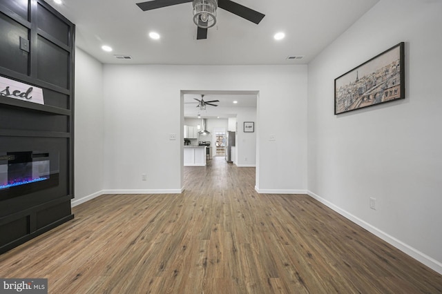 unfurnished living room featuring a fireplace, dark wood-type flooring, and ceiling fan