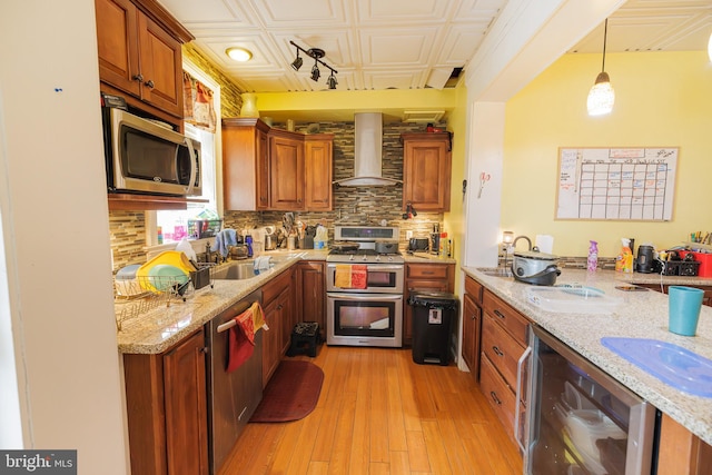 kitchen featuring wall chimney exhaust hood, sink, decorative light fixtures, appliances with stainless steel finishes, and beverage cooler