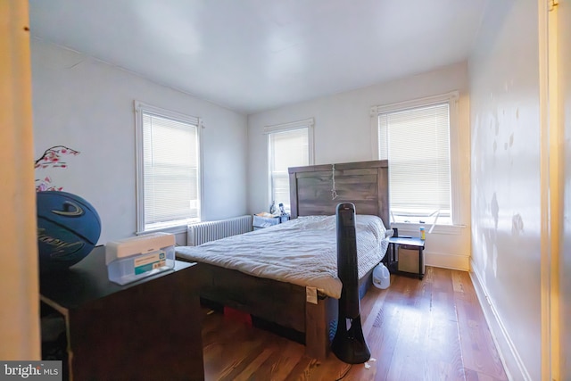 bedroom with multiple windows, hardwood / wood-style flooring, and radiator heating unit