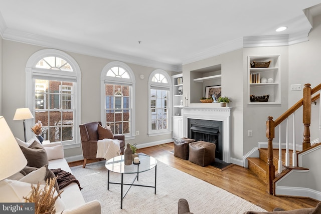 living room with crown molding, built in features, and light hardwood / wood-style floors