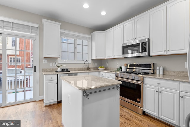 kitchen with sink, white cabinets, light stone counters, a kitchen island, and stainless steel appliances