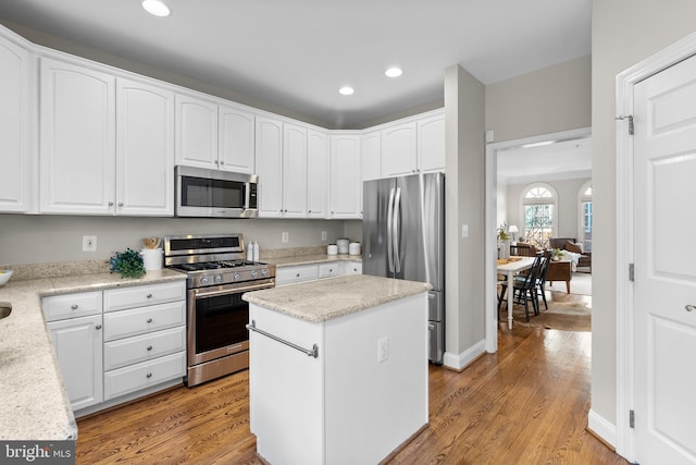 kitchen featuring white cabinets, appliances with stainless steel finishes, a kitchen island, light stone counters, and light hardwood / wood-style flooring